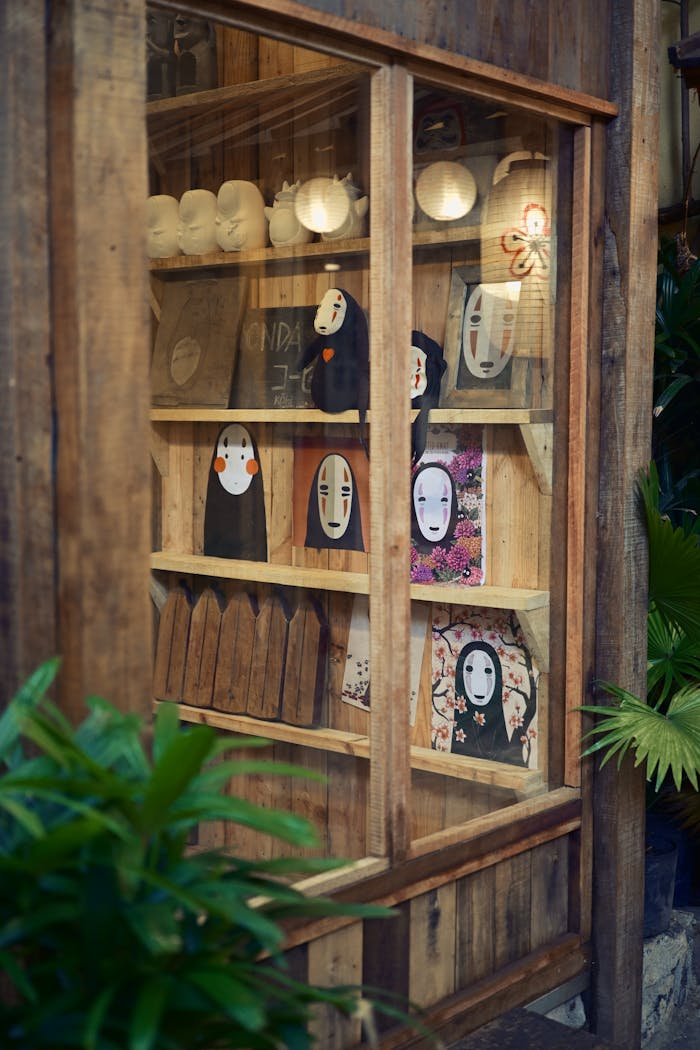 services-img Showcase of Japanese anime items in a rustic wooden cabinet, surrounded by plants.