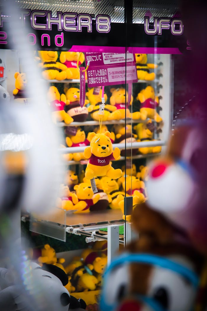 Vibrant claw machine filled with Winnie the Pooh plush toys in a Japanese arcade.